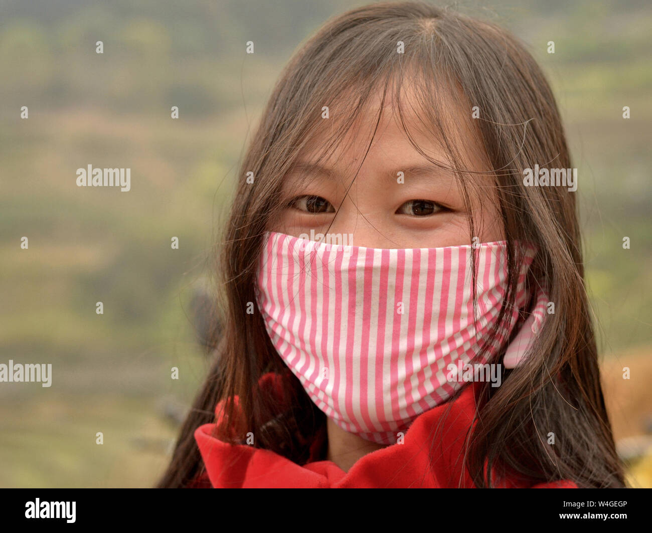 Young Vietnamese woman with beautiful oriental eyes covers her nose and mouth with a striped protective face mask. Stock Photo