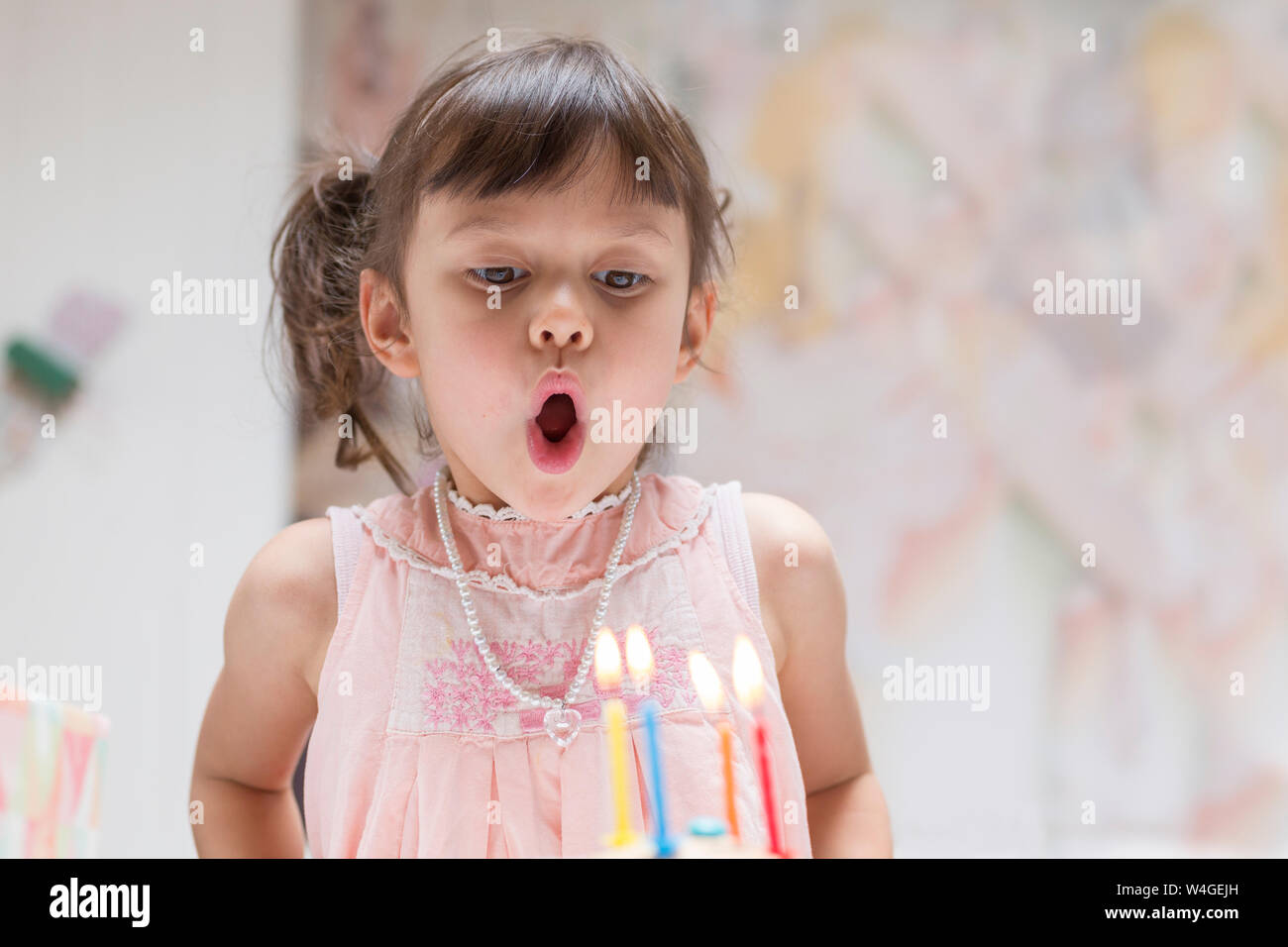Portrait of little girl blowing out burning candles on her birthday cake Stock Photo