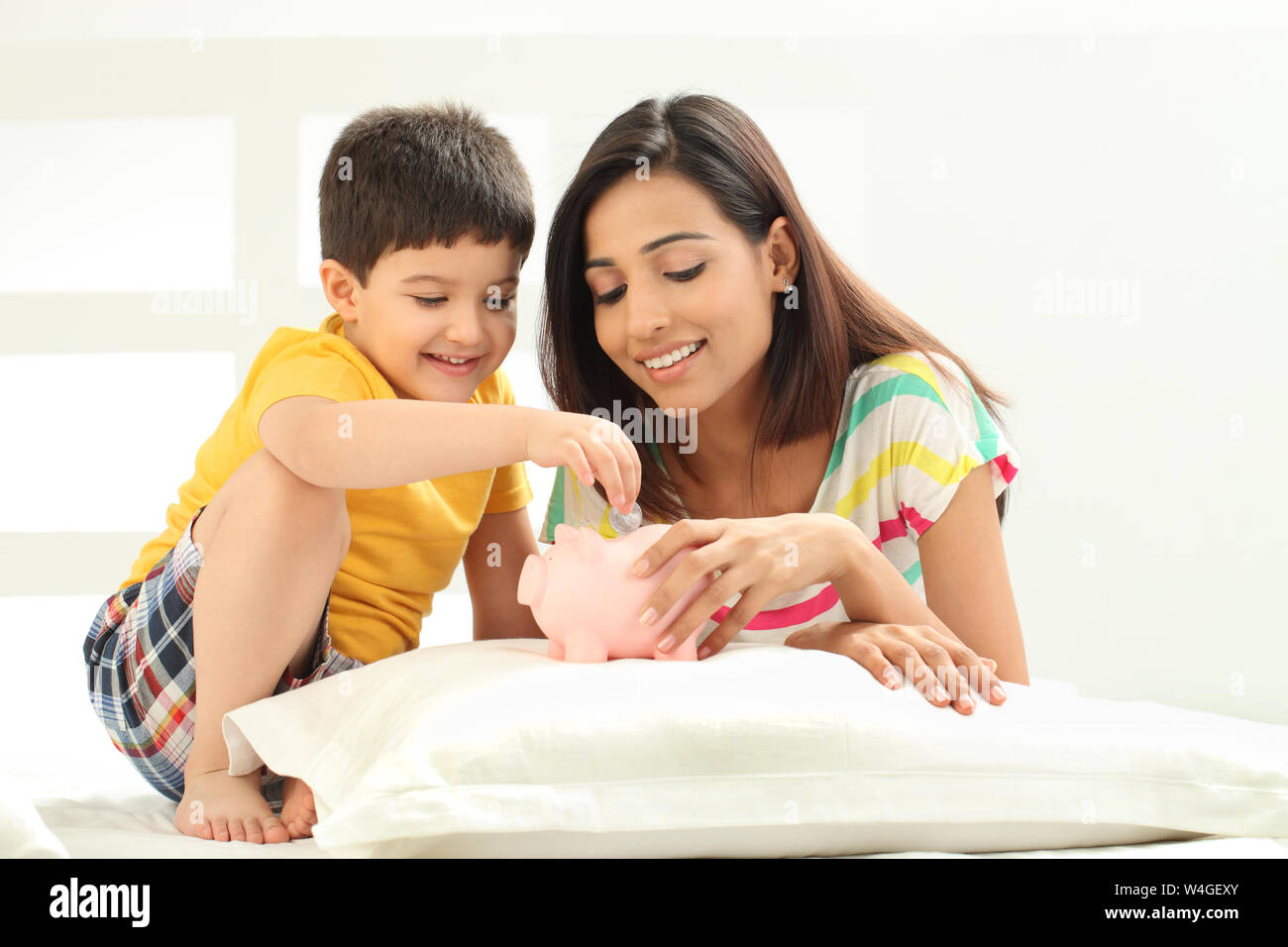 Boy putting coin into a piggy bank with his mother Stock Photo - Alamy