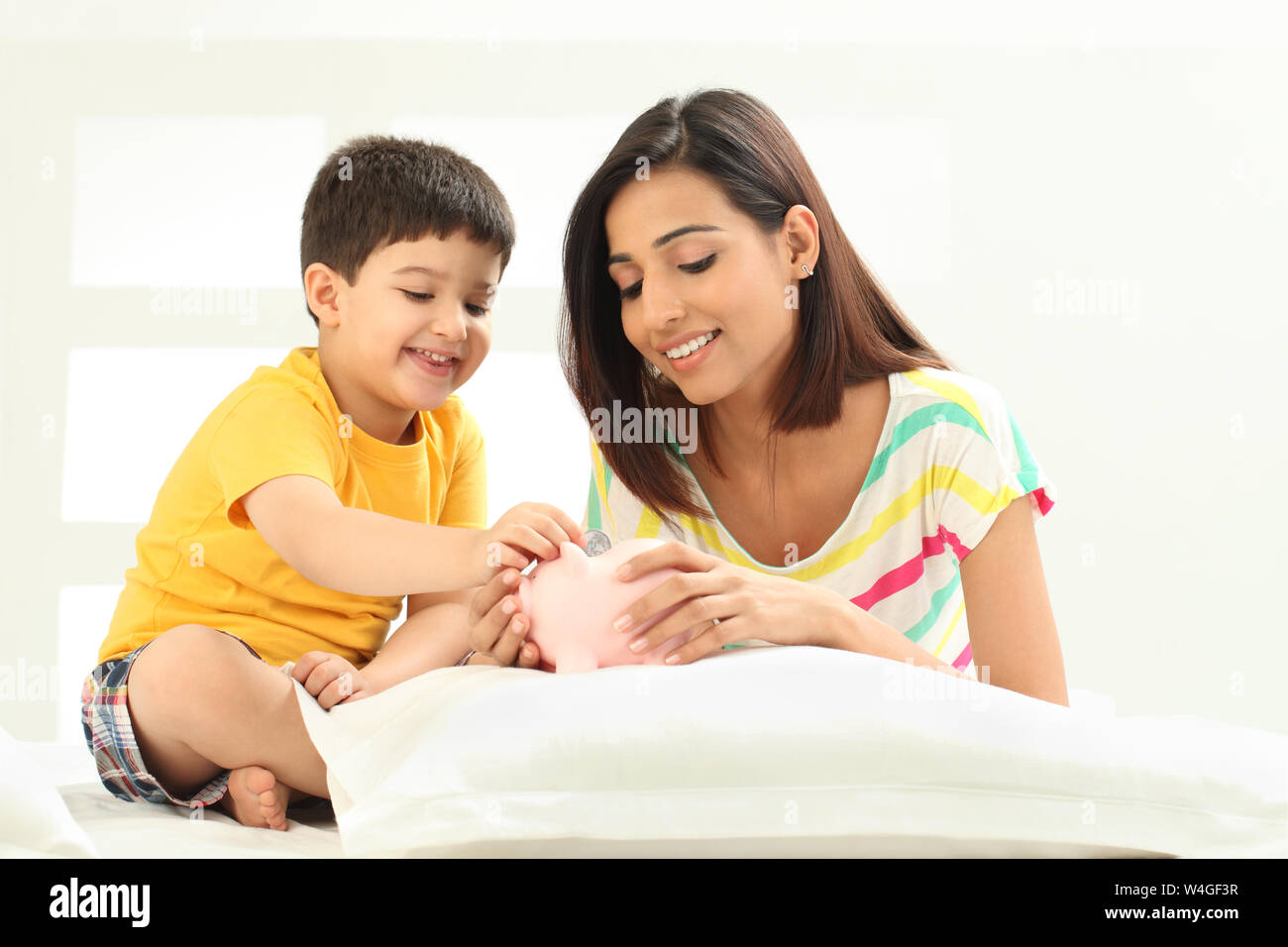 Boy putting coin into a piggy bank with his mother Stock Photo - Alamy