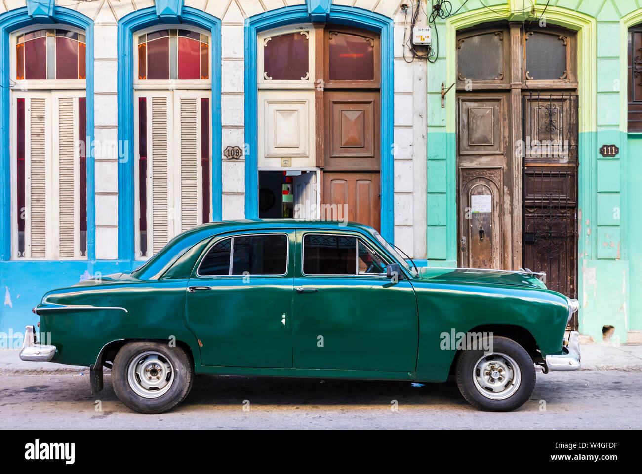 Green vintage car parked in front of house entrances, Havana, Cuba Stock Photo