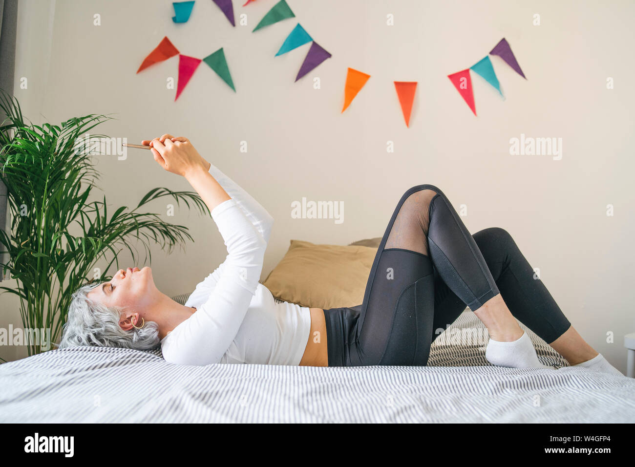 Woman lying on bed at home taking a selfie Stock Photo