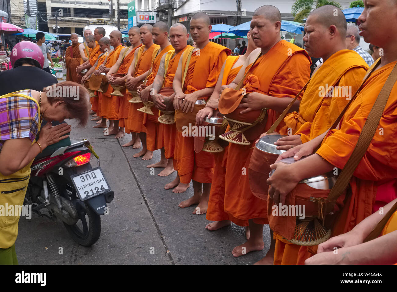 A market vendor in Phuket Town, Thailand,  bows to and greets Buddhist monks with a traditional 'wai', the monks on their ritual morning alms round Stock Photo