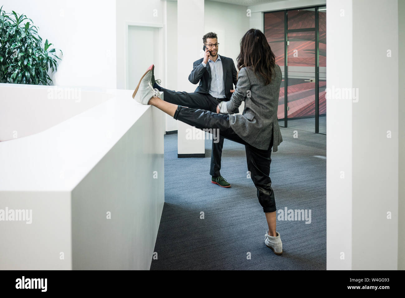 Businessman and woman standing on one leg in office Stock Photo