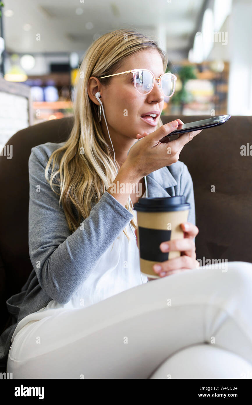 Young woman talking on mobile phone with hands free while drinking a coffee in a coffee shop Stock Photo