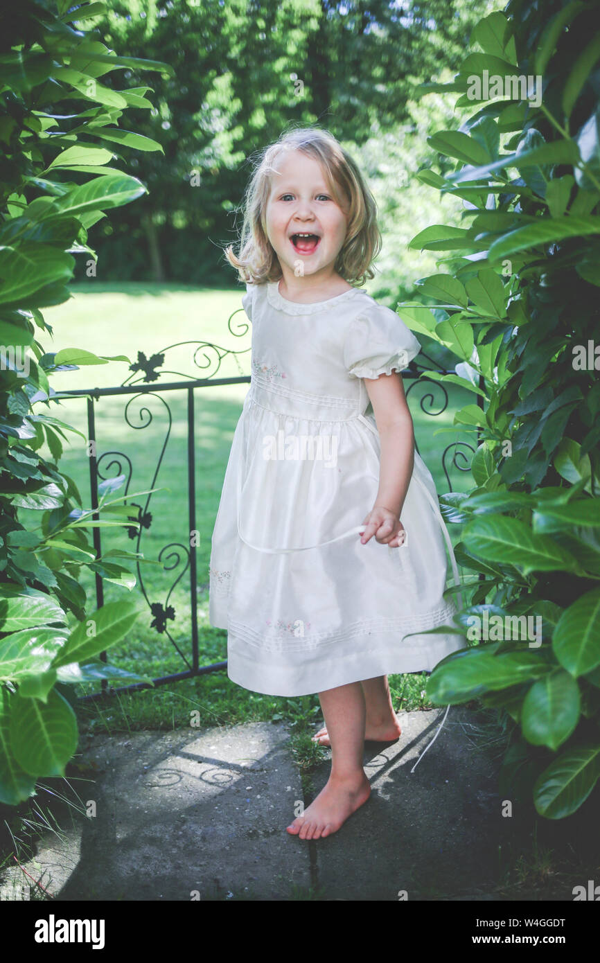 https://c8.alamy.com/comp/W4GGDT/portrait-of-happy-little-girl-wearing-white-dress-standing-near-garden-gate-W4GGDT.jpg