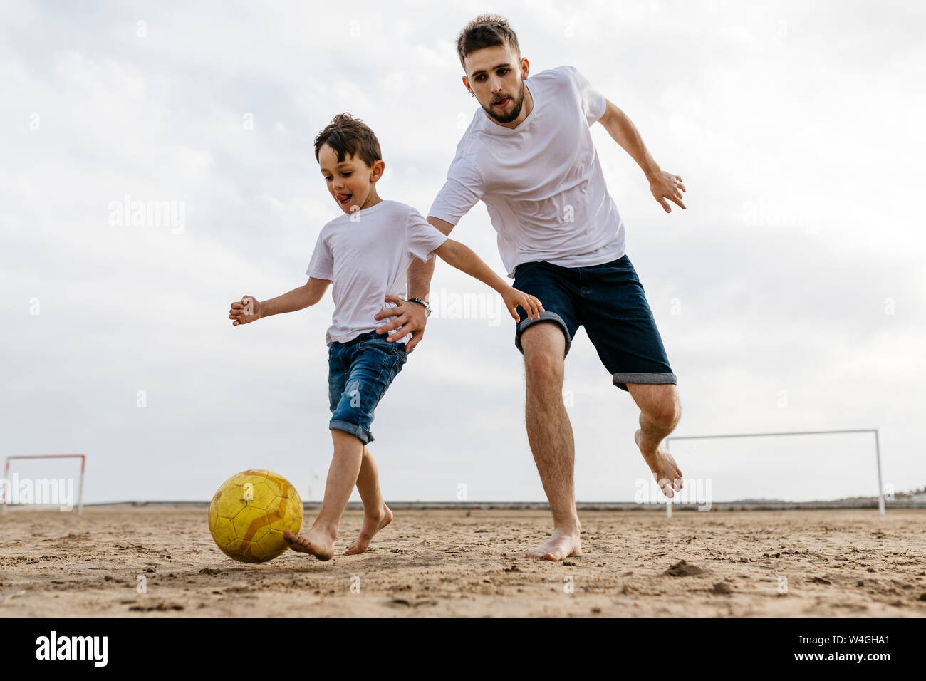 Boy and man playing soccer on the beach Stock Photo