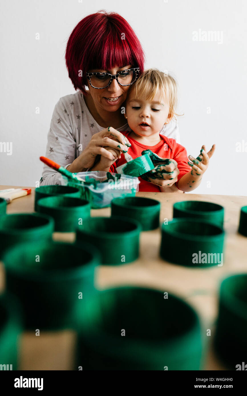 Mother and daughter doing crafts at home, painting cardboard rolls to make a Christmas tree Stock Photo