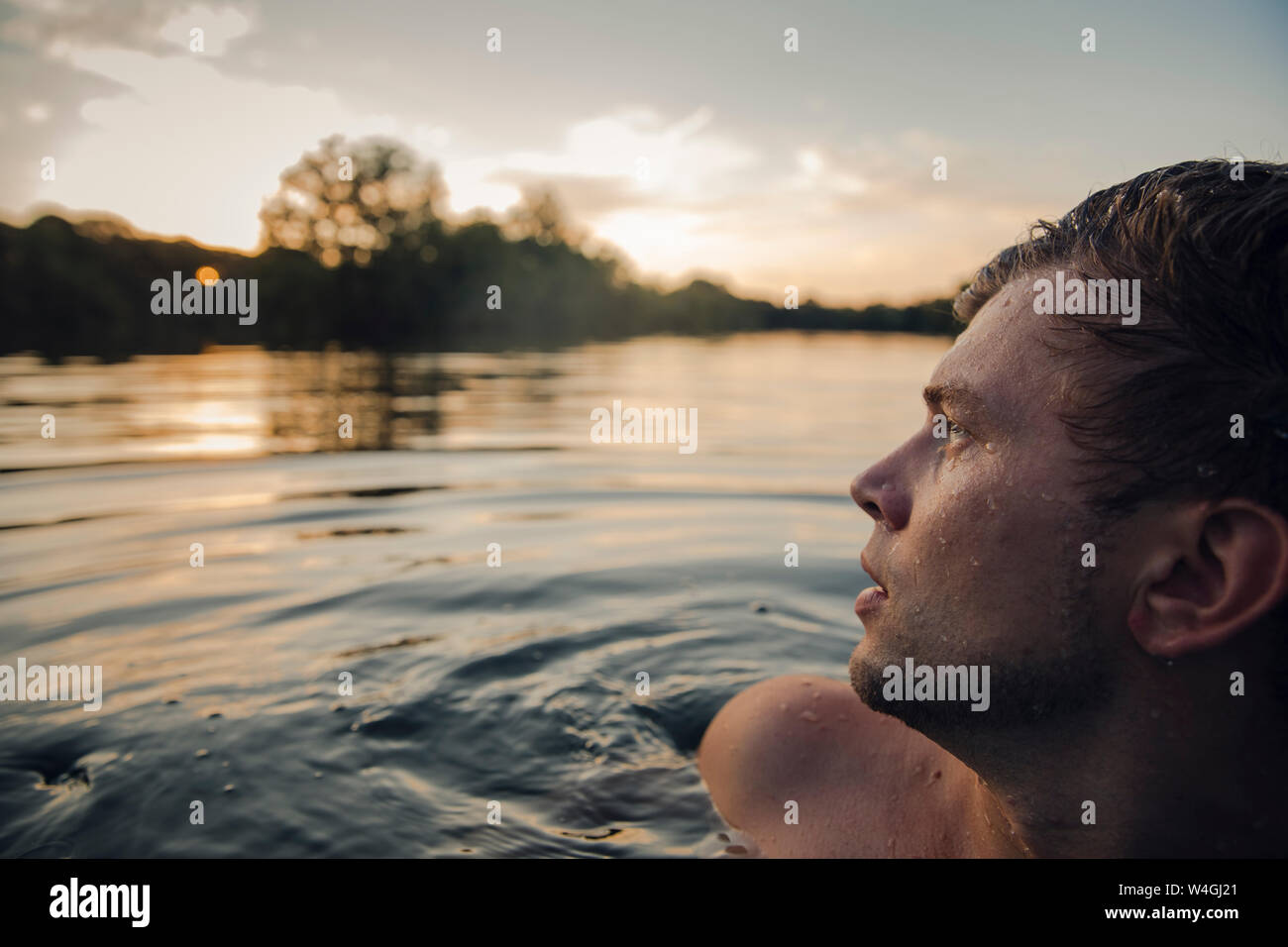 Young man swimming in lake, watching sunset Stock Photo