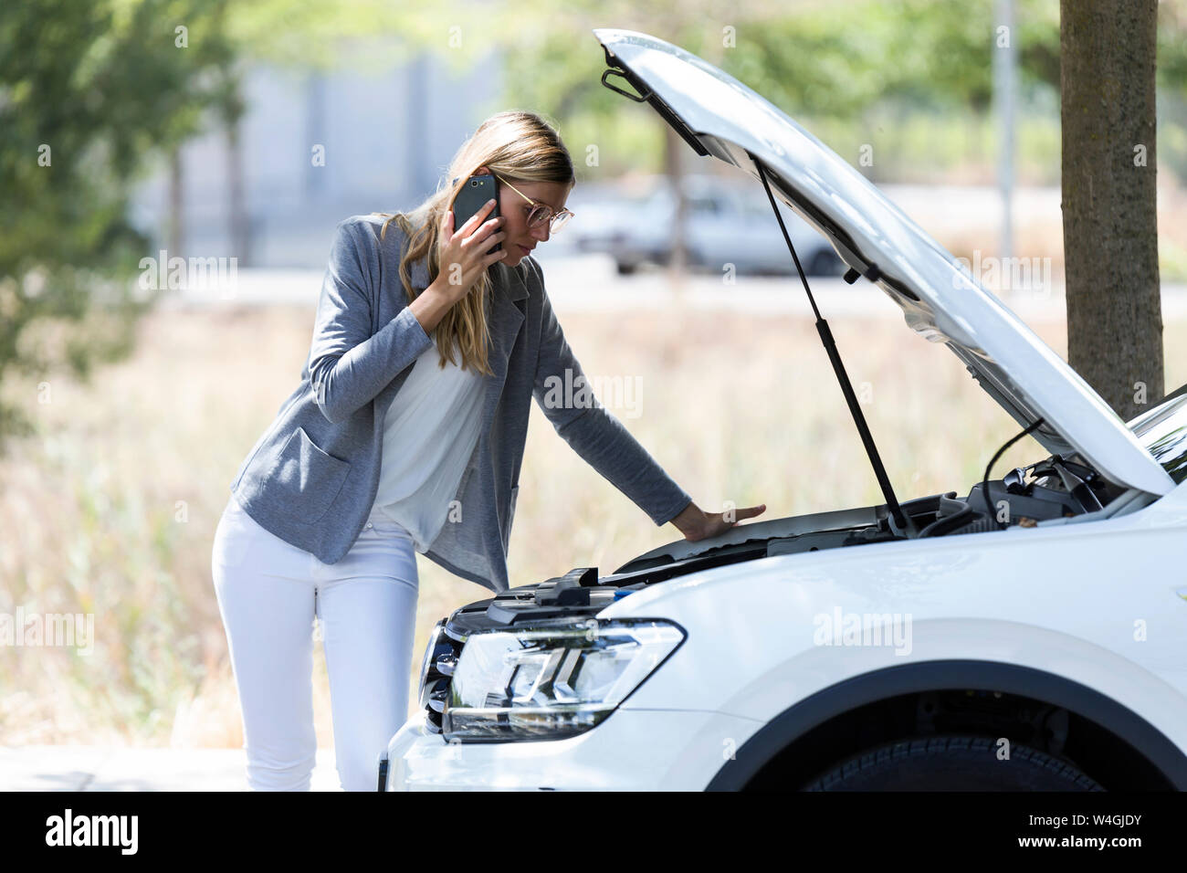 Stressed young woman calling for assistance after breaking down car Stock Photo