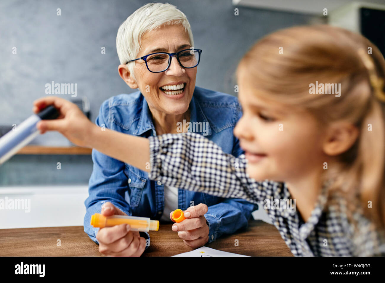 Grandmother and granddaughter sitting at table, painting colouring book Stock Photo