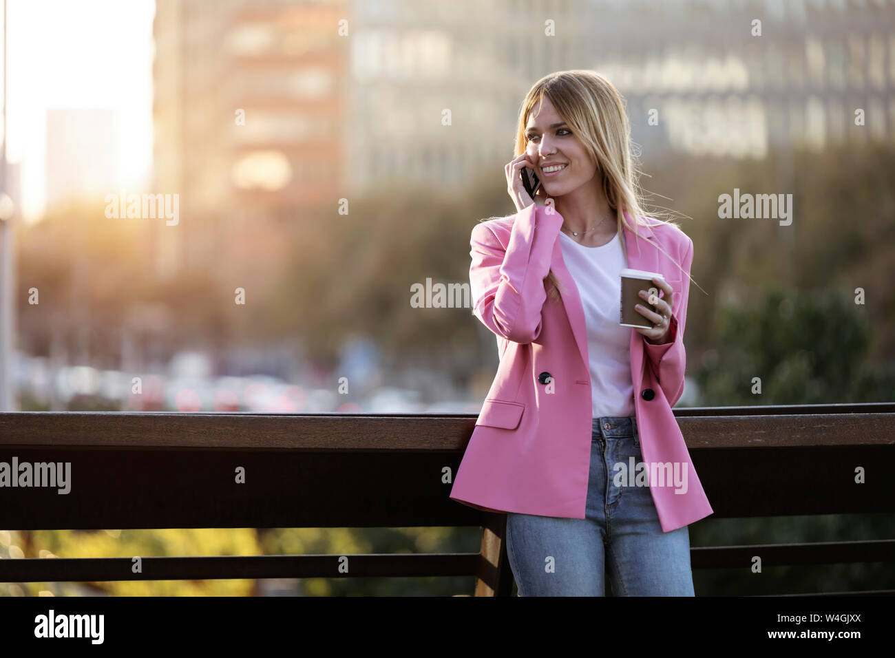 Young businesswoman using smartphone and holding coffee to go Stock Photo