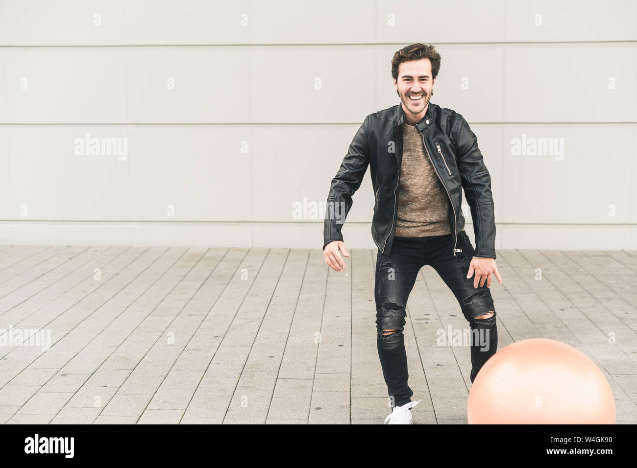 Young man in leather jacket, playing with a gym ball Stock Photo