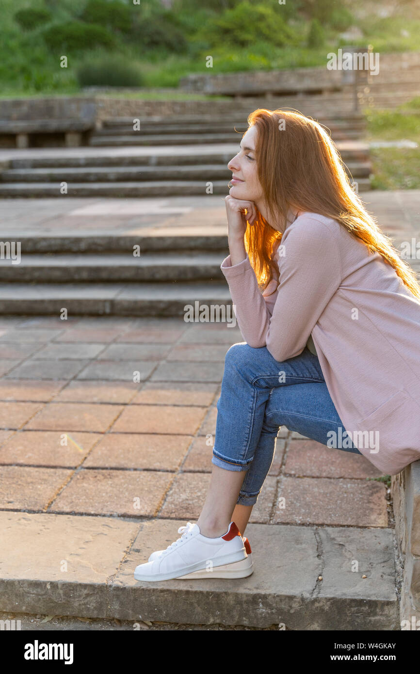 Young redheaded woman sitting in a park Stock Photo - Alamy