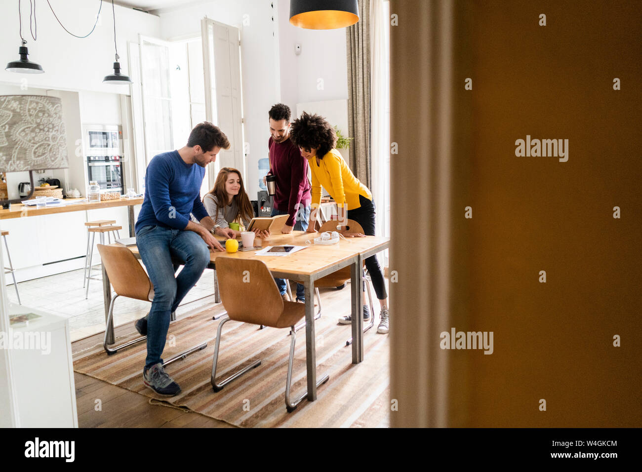 Four friends in dining room at home with book Stock Photo