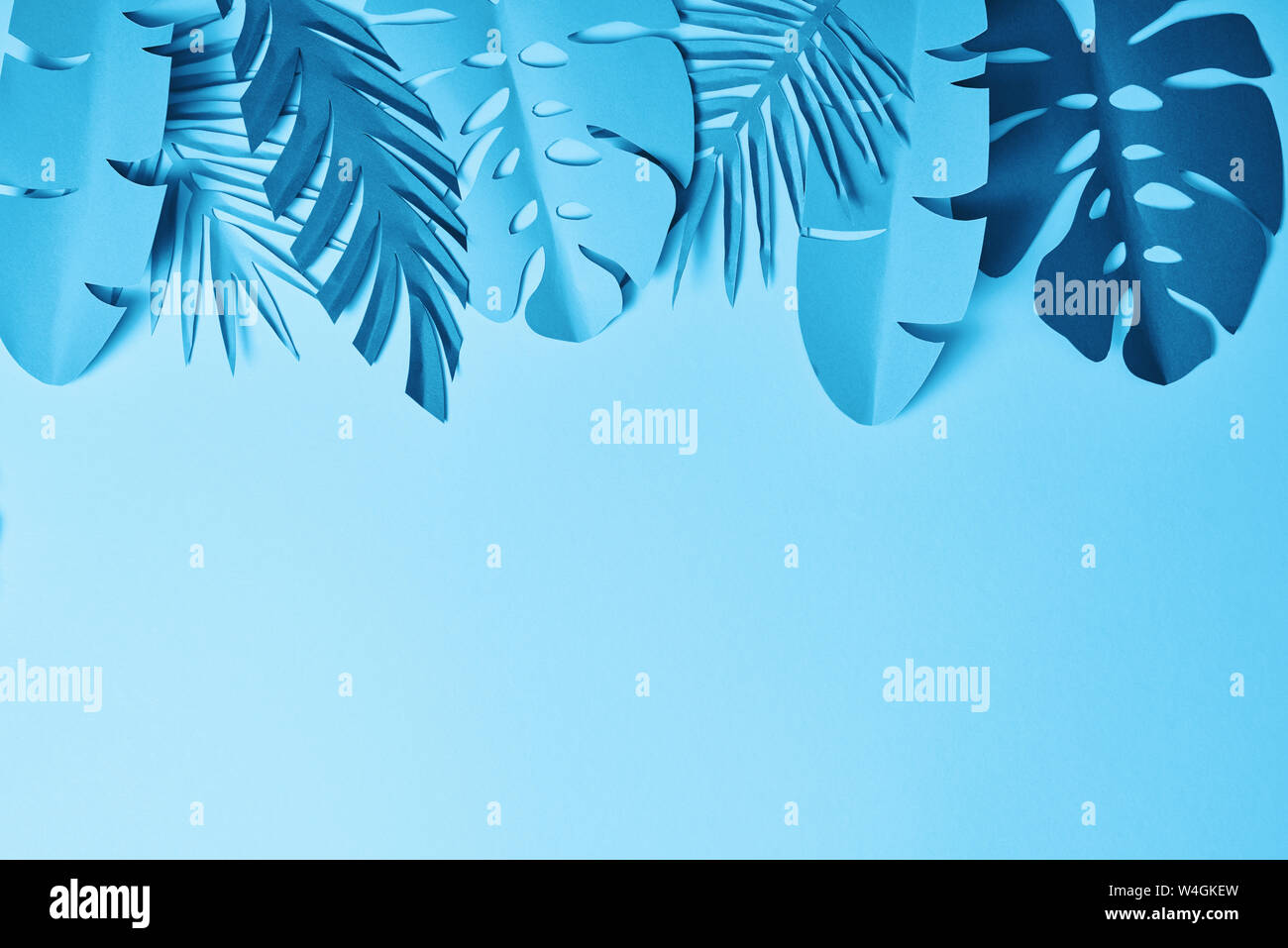 top view of blue exotic paper cut palm leaves on blue background with ...