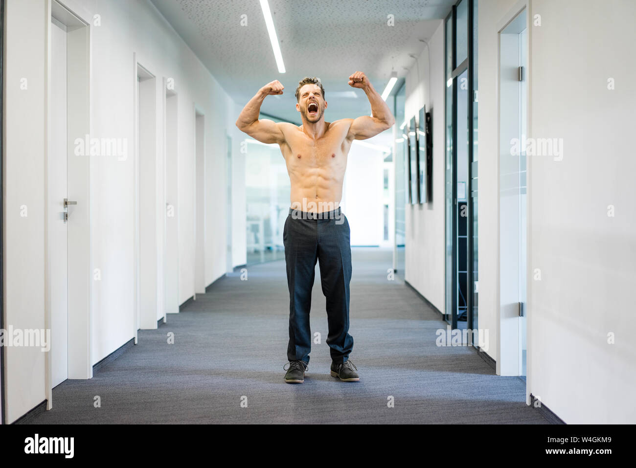 Screaming barechested businessman flexing muscles in office Stock Photo