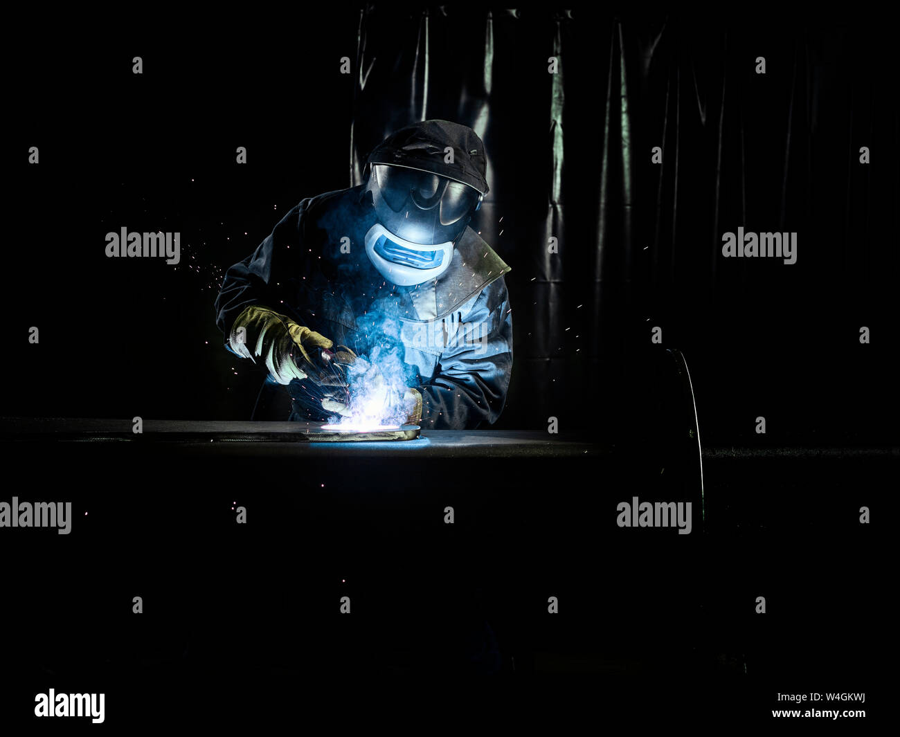 Industrial worker in protective clothing welding metal with welding torch Stock Photo