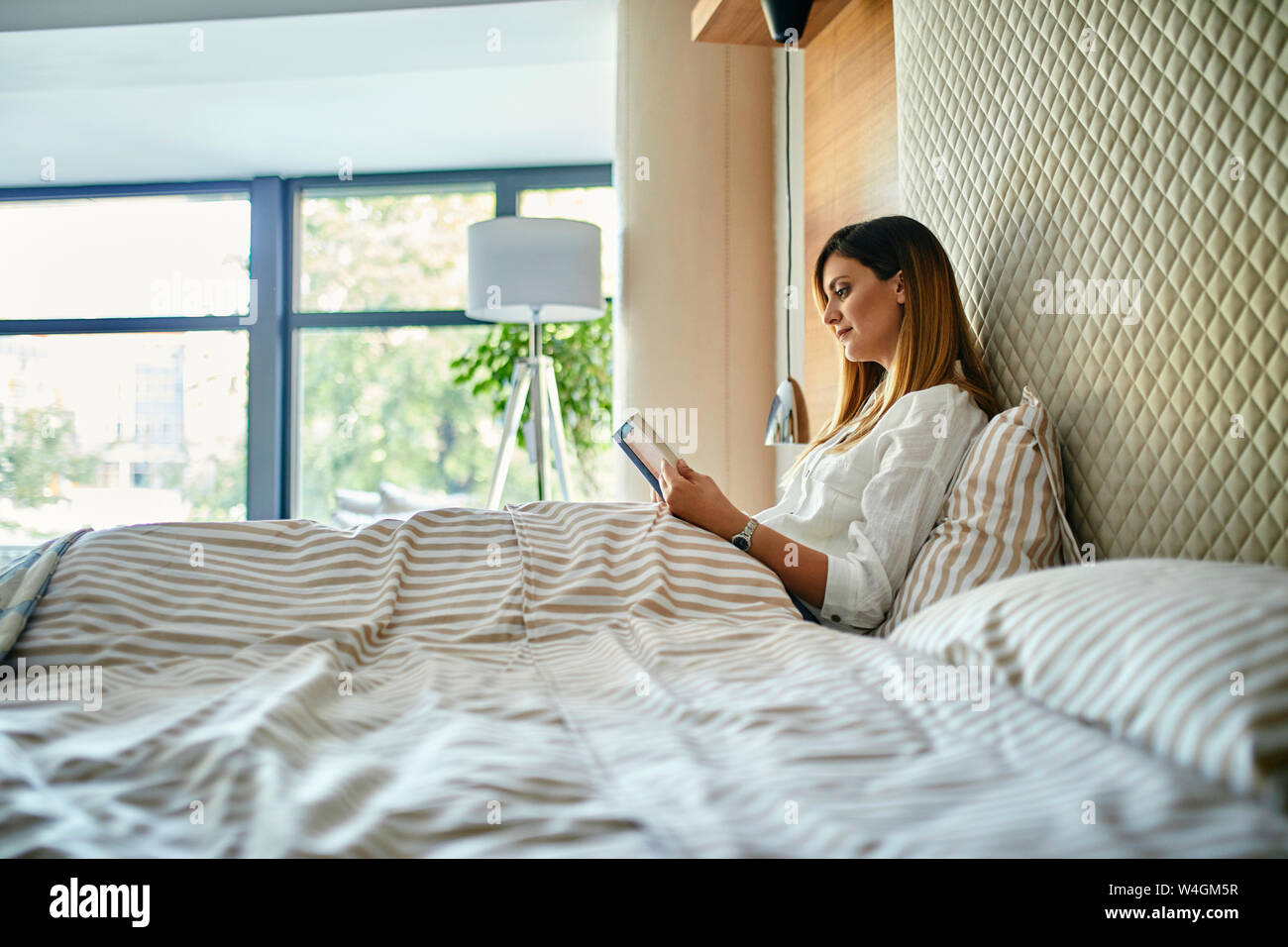 Woman sitting in bed, reading a book Stock Photo