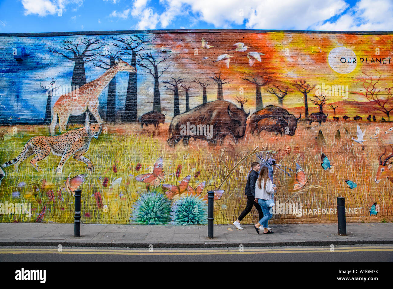People passing by the graffiti wall art at Brick Lane Market in London, United Kingdom Stock Photo