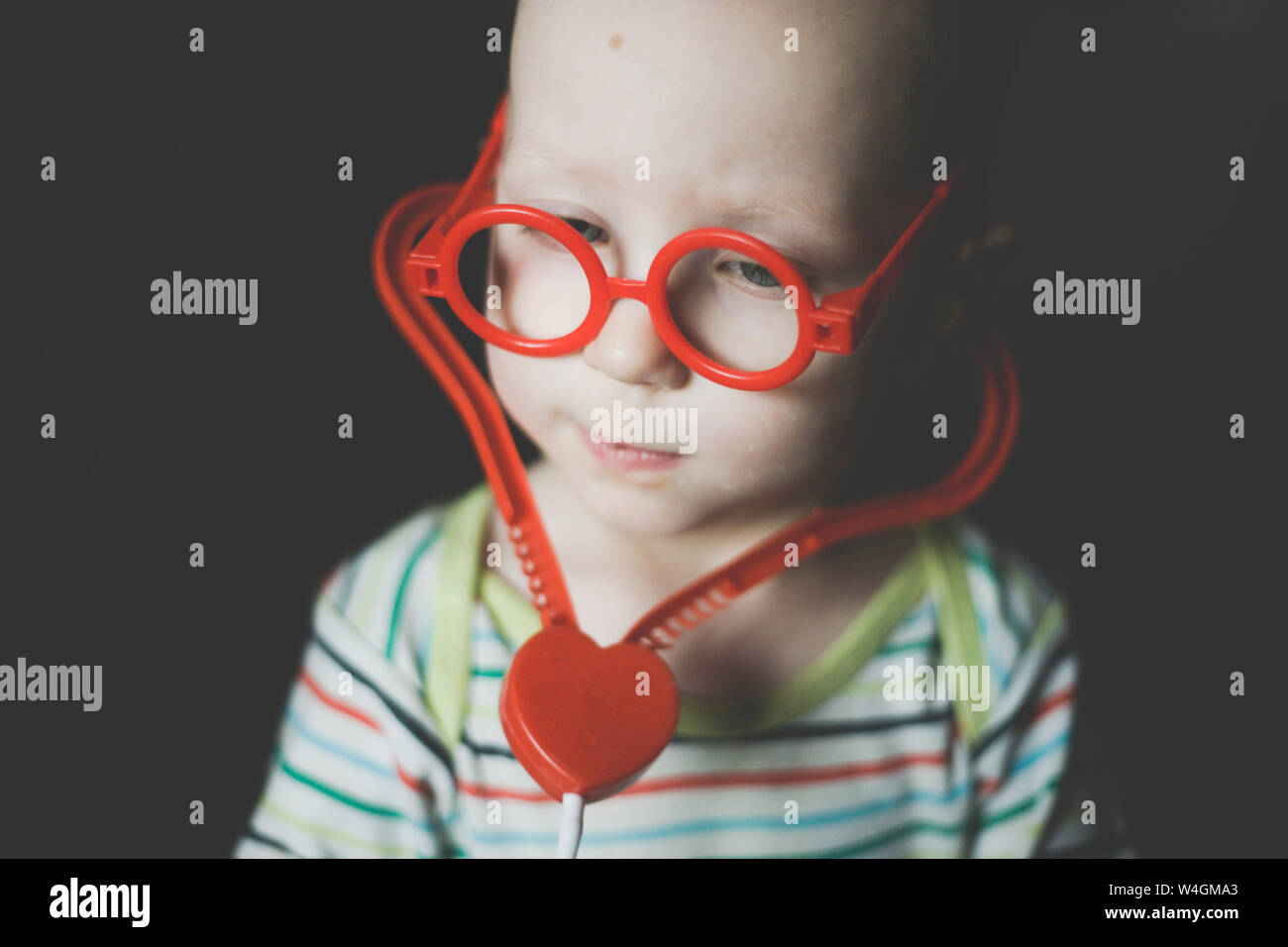 Portrait of toddler boy wearing oversized red toy glasses and toy stethoscope Stock Photo