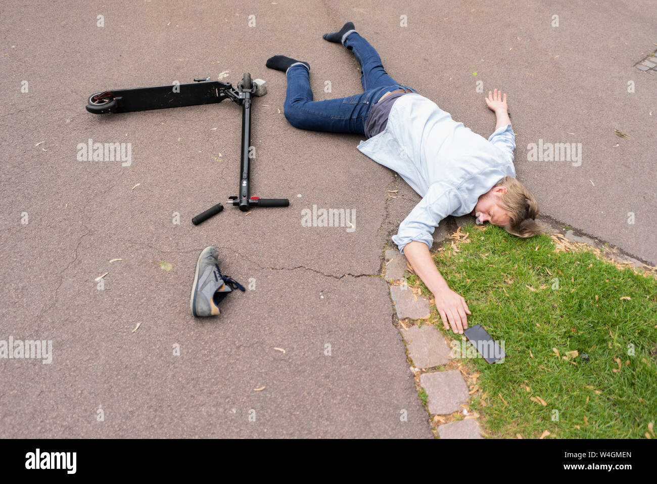 Accident victim lying on road besides E-Scooter and smartphone Stock Photo