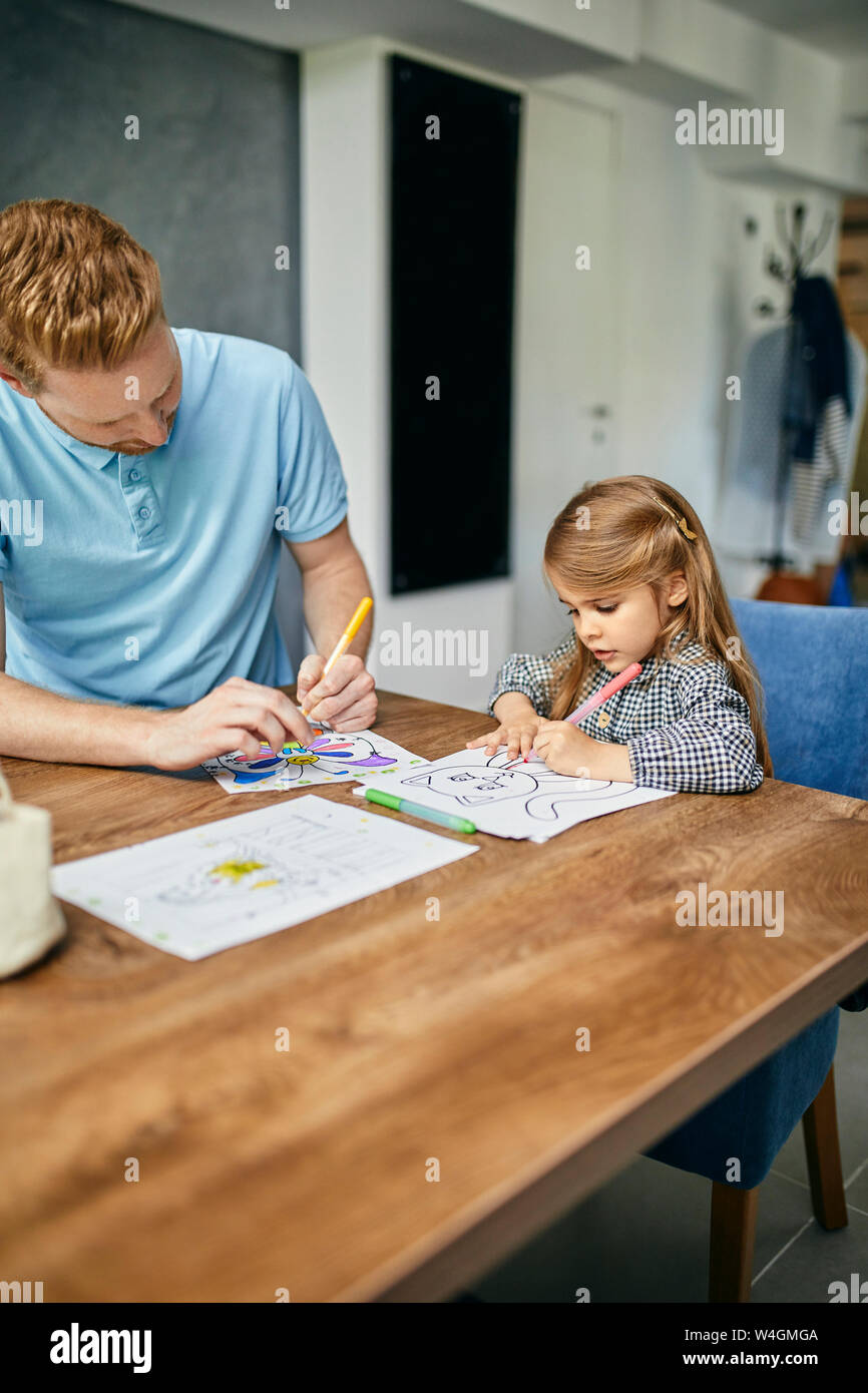 Father and daughter sitting at table, painting colouring book Stock Photo