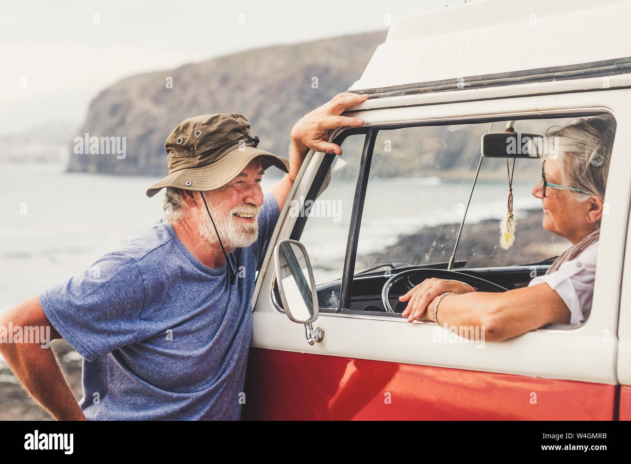 Senior couple traveling in a vintage van, taking a break at the sea, talking Stock Photo
