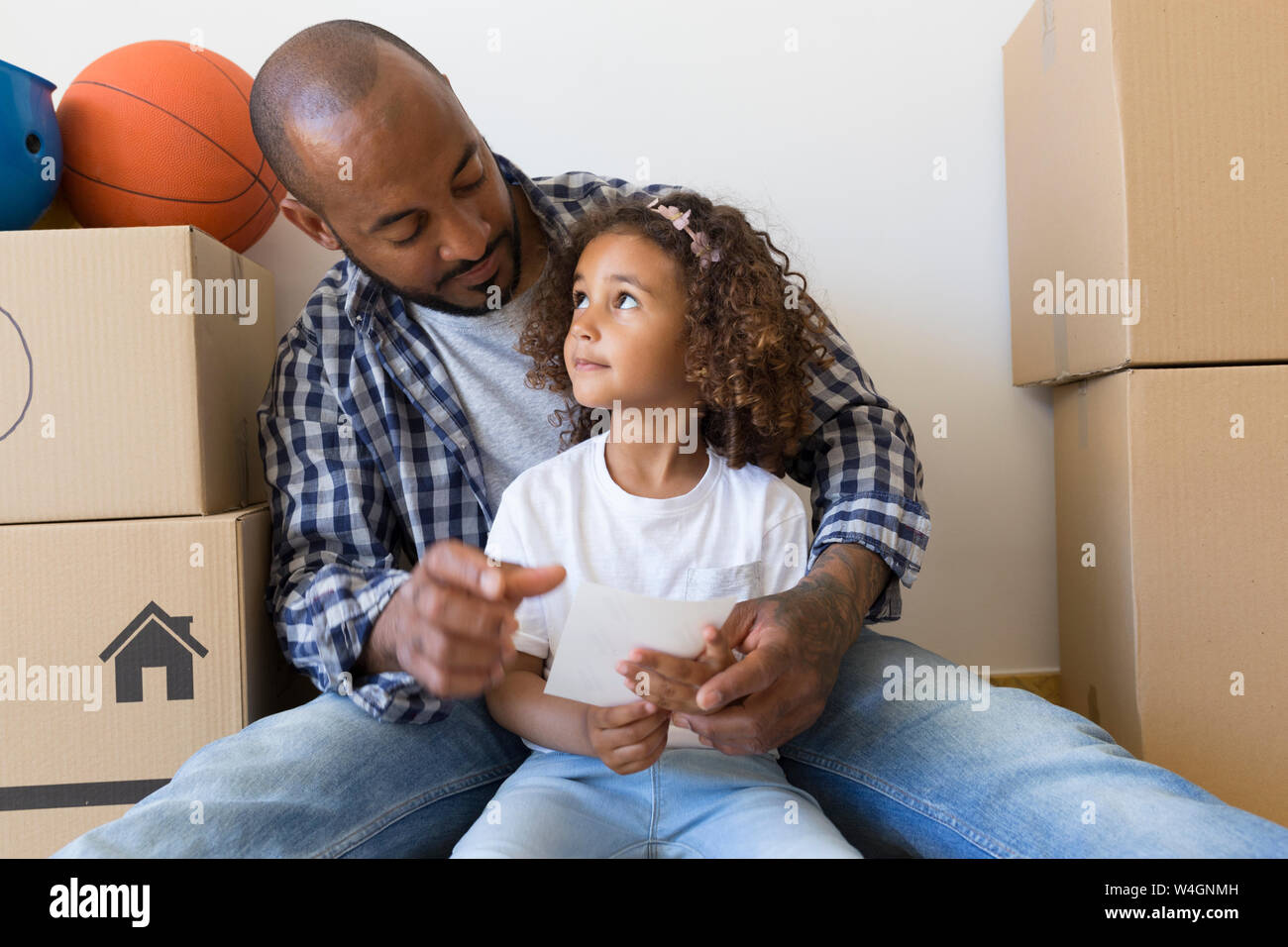 Father and daughter sitting on the floor at new home surrounded by cardboard boxes Stock Photo
