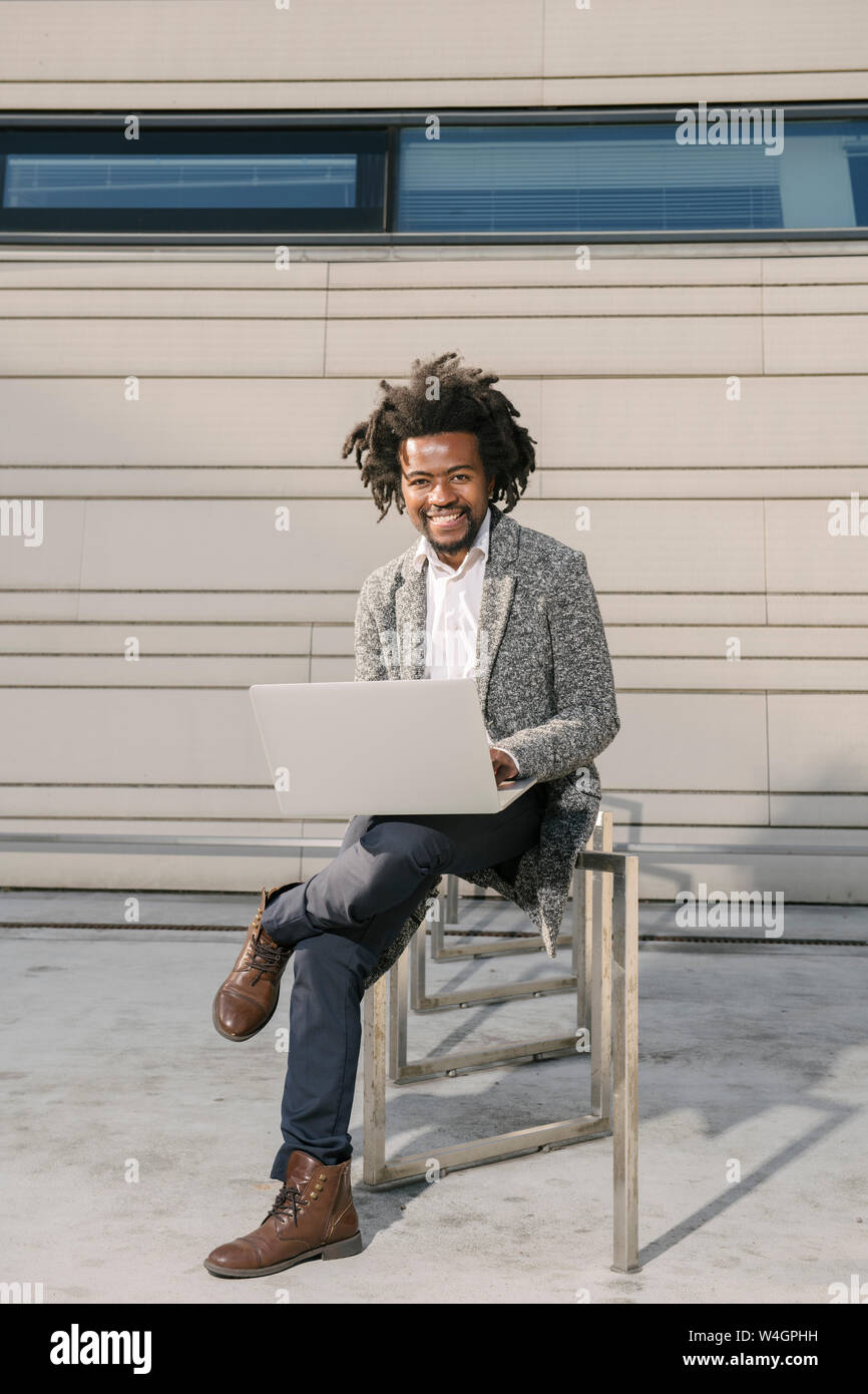 Portrait of smiling businessman on bicycle stand outside office using laptop Stock Photo