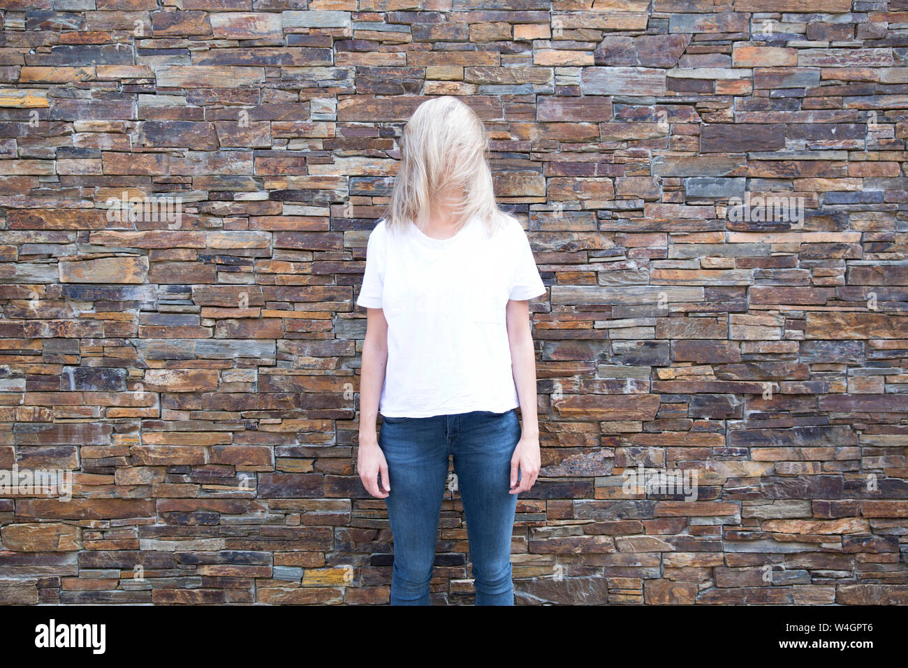 Woman in front of stone wall, obscured face Stock Photo
