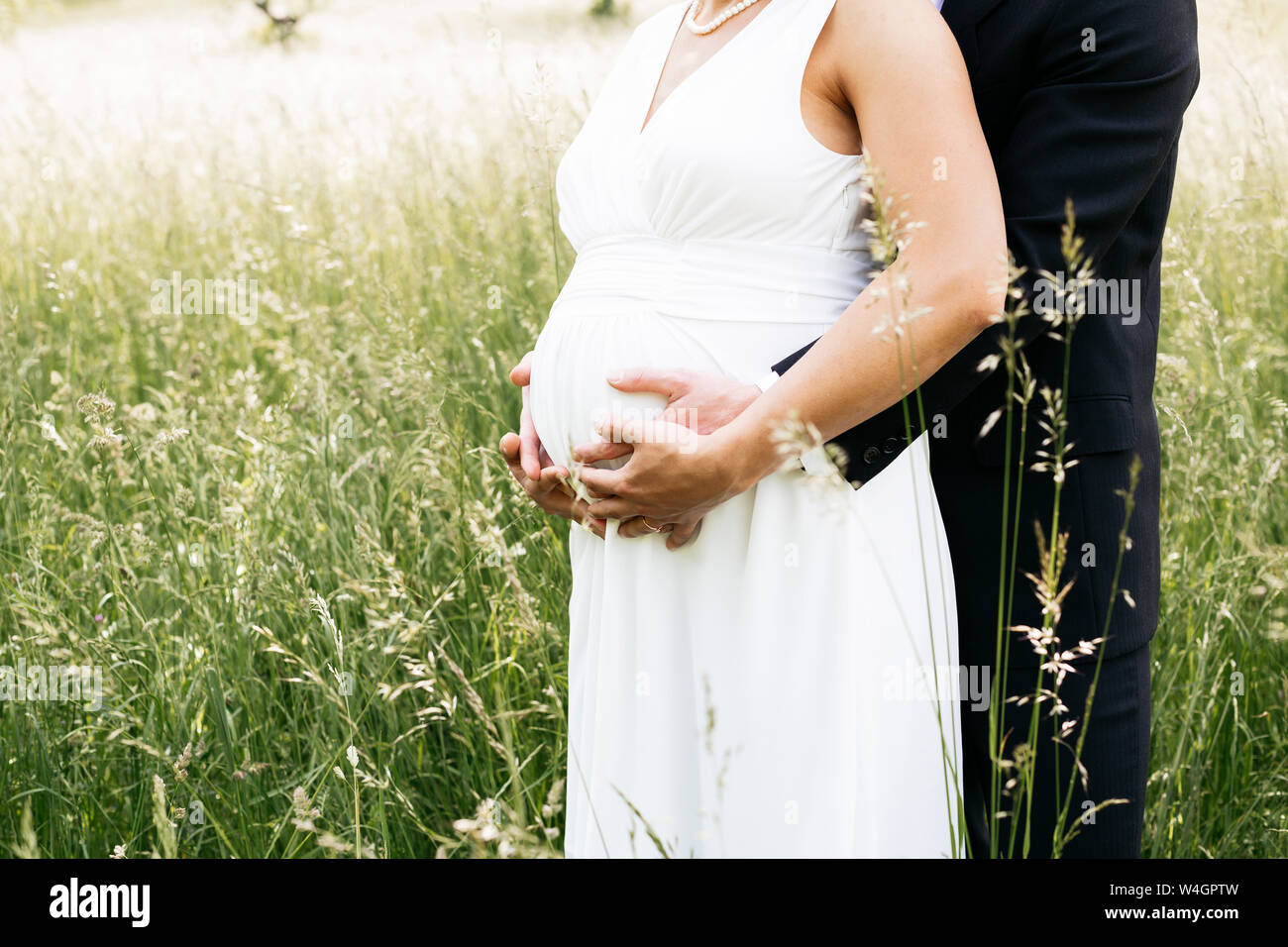 Pregnant bride with her husband holding baby belly on a meadow Stock Photo