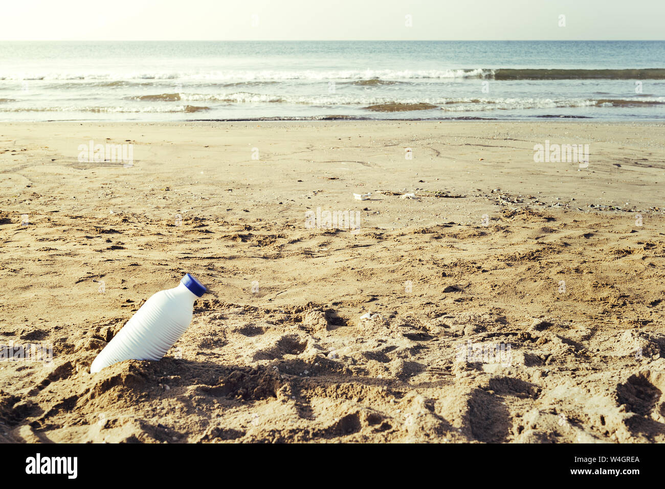 white plastic bottle lying on the shore of the beach and pollutes the sea and the marine life, concept of pollution control of the oceans by plastic Stock Photo