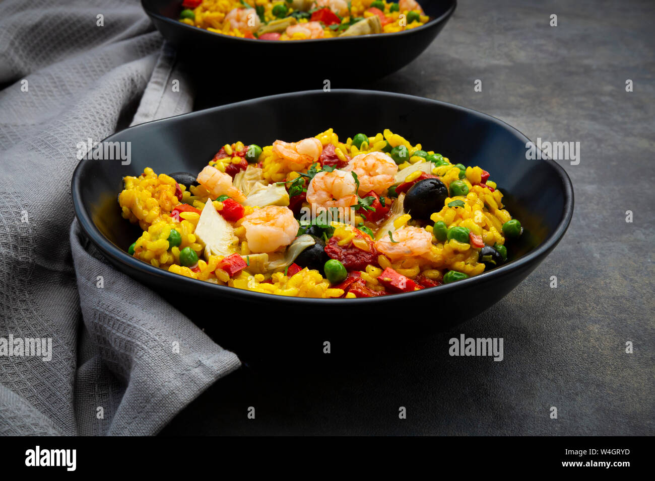 Paella with rice, bell pepper, tomato, artichoke, pea, black olive, curcuma and shrimps Stock Photo