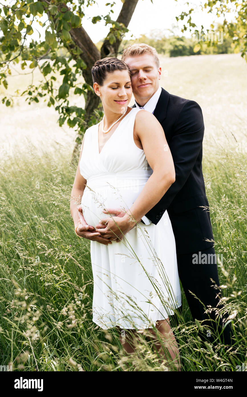 Pregnant bride with his husband holding baby belly on a meadow Stock Photo