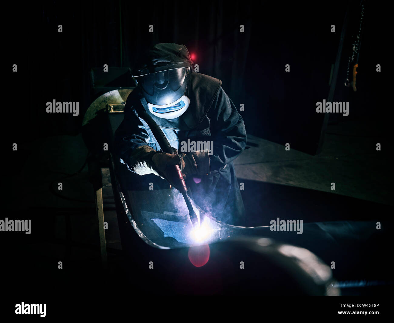 Industrial worker in protective clothing welding metal with welding torch Stock Photo