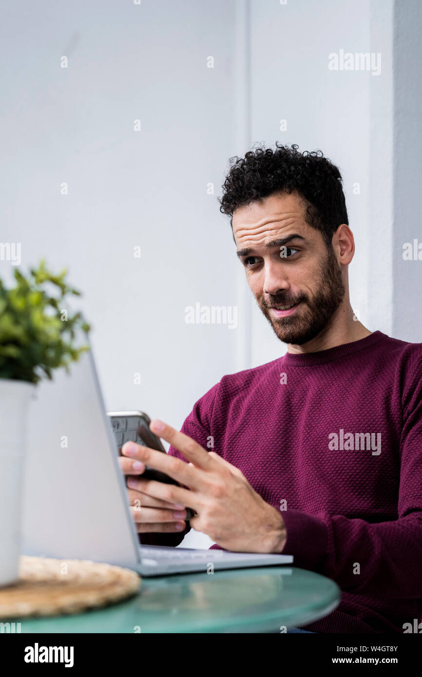 Young man stting at table at home using laptop and cell phone Stock Photo
