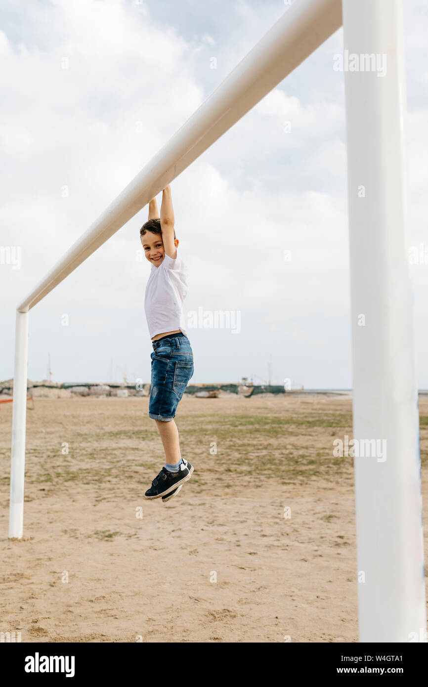 Boy hanging from the goal on the beach Stock Photo
