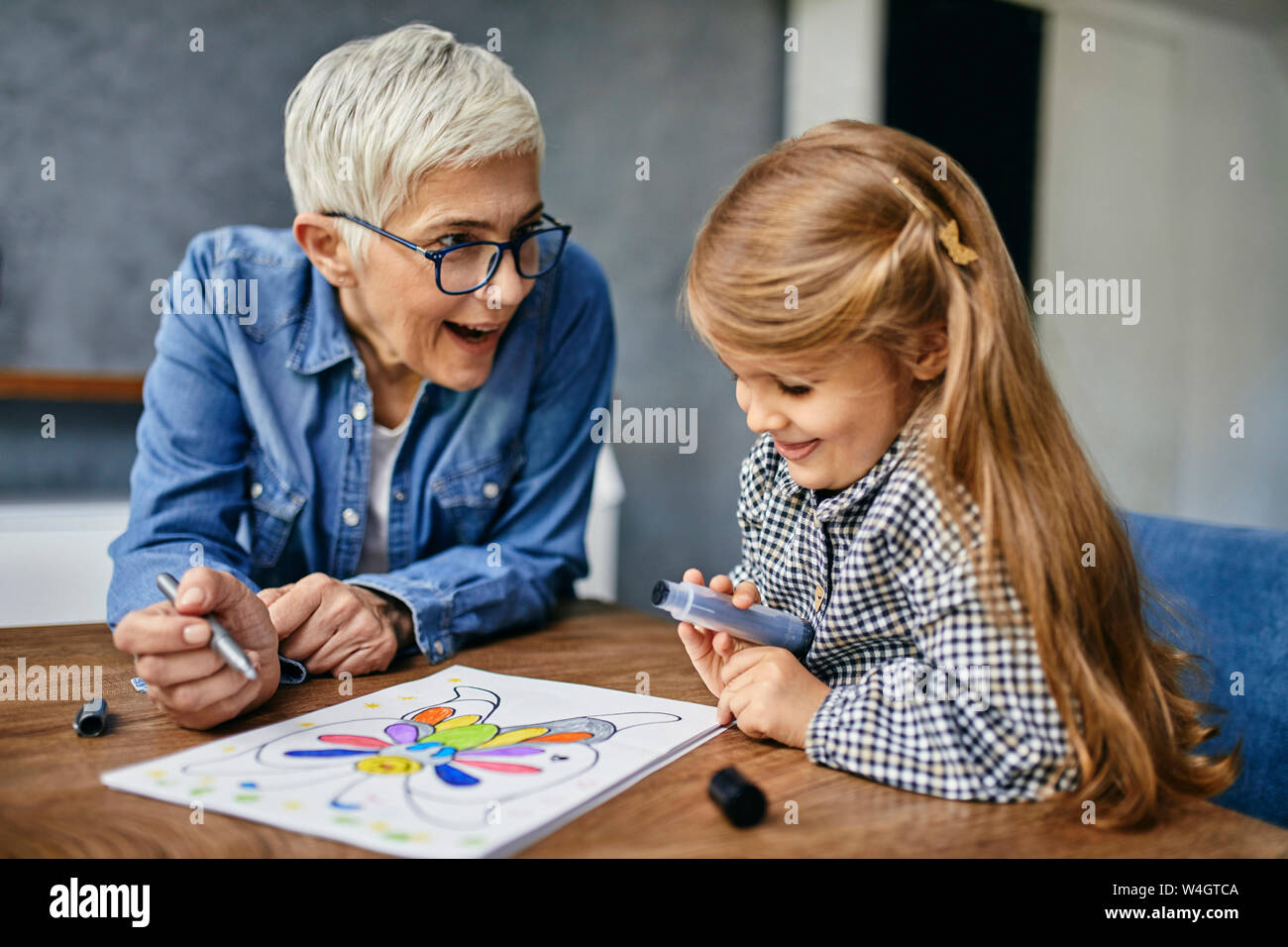 Grandmother and granddaughter sitting at table, painting colouring book Stock Photo