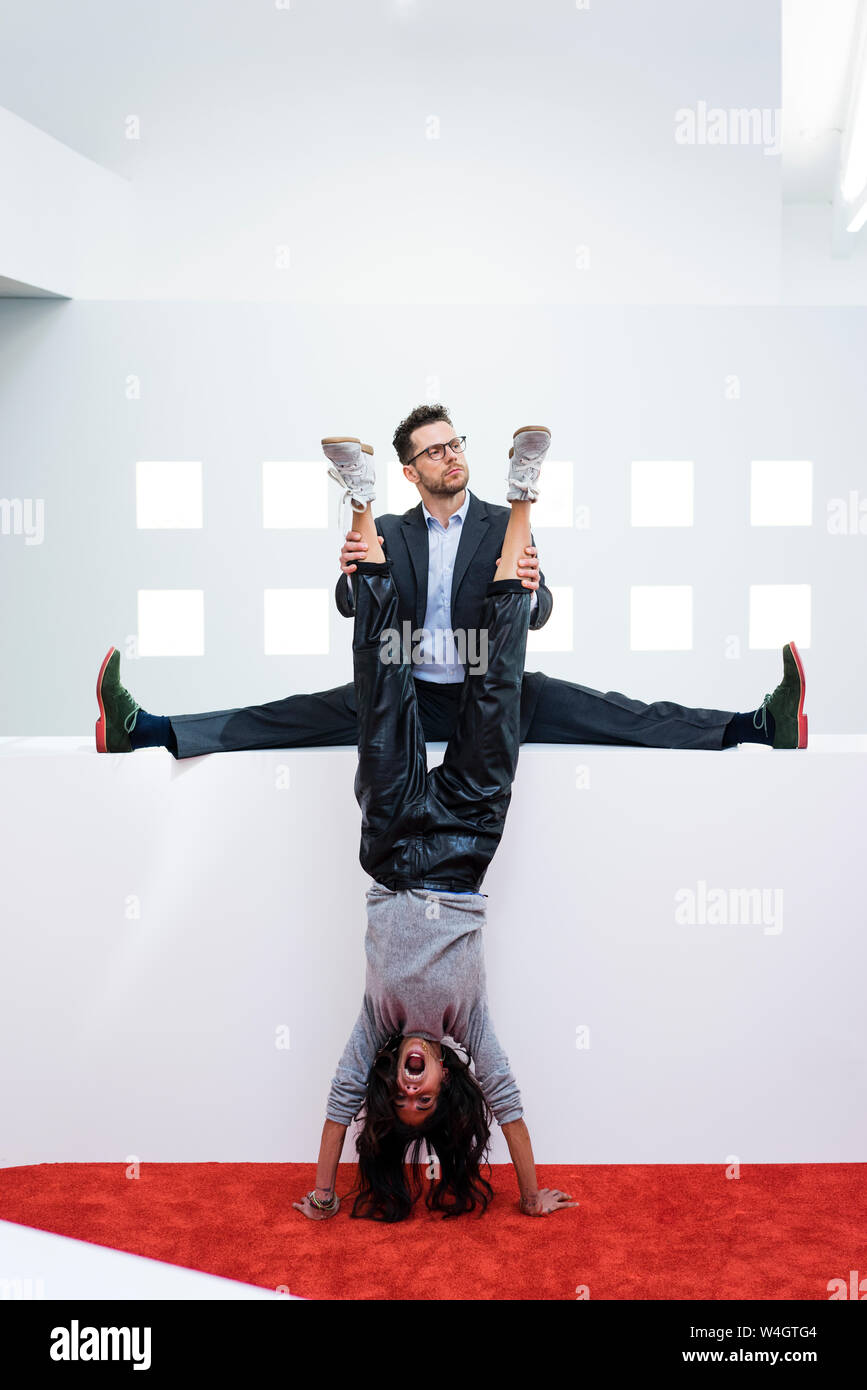 Businessman in office holding woman's legs doing a handstand Stock Photo