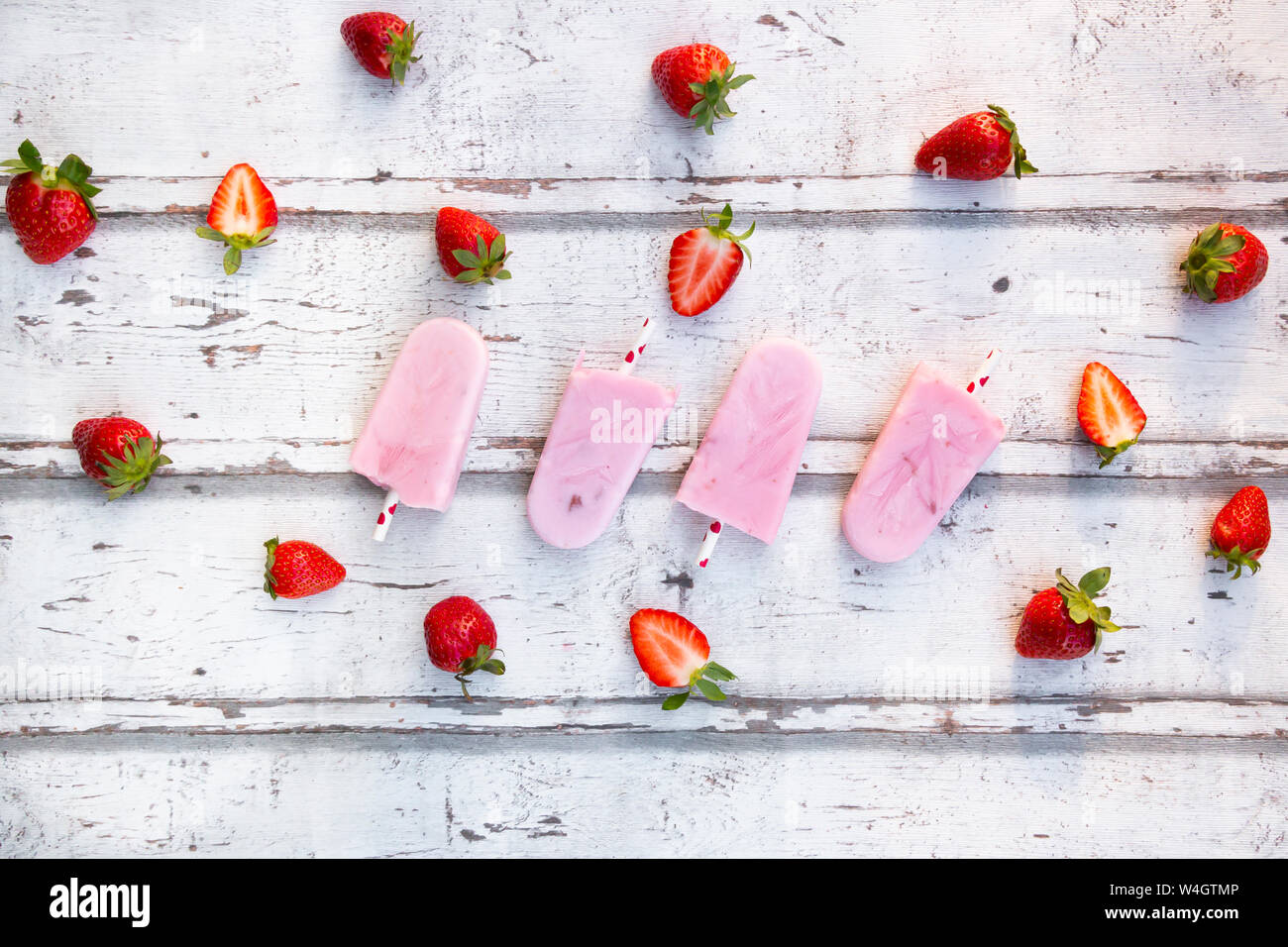 Homemade strawberry yogurt ice lollies with fresh strawberries on white