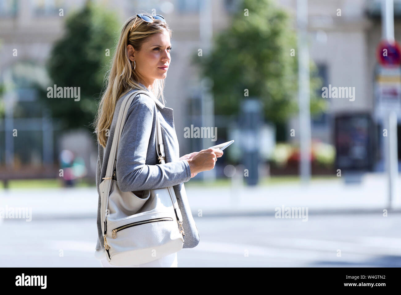 Young businesswoman working with digital tablet while standing with suitcase in the street Stock Photo