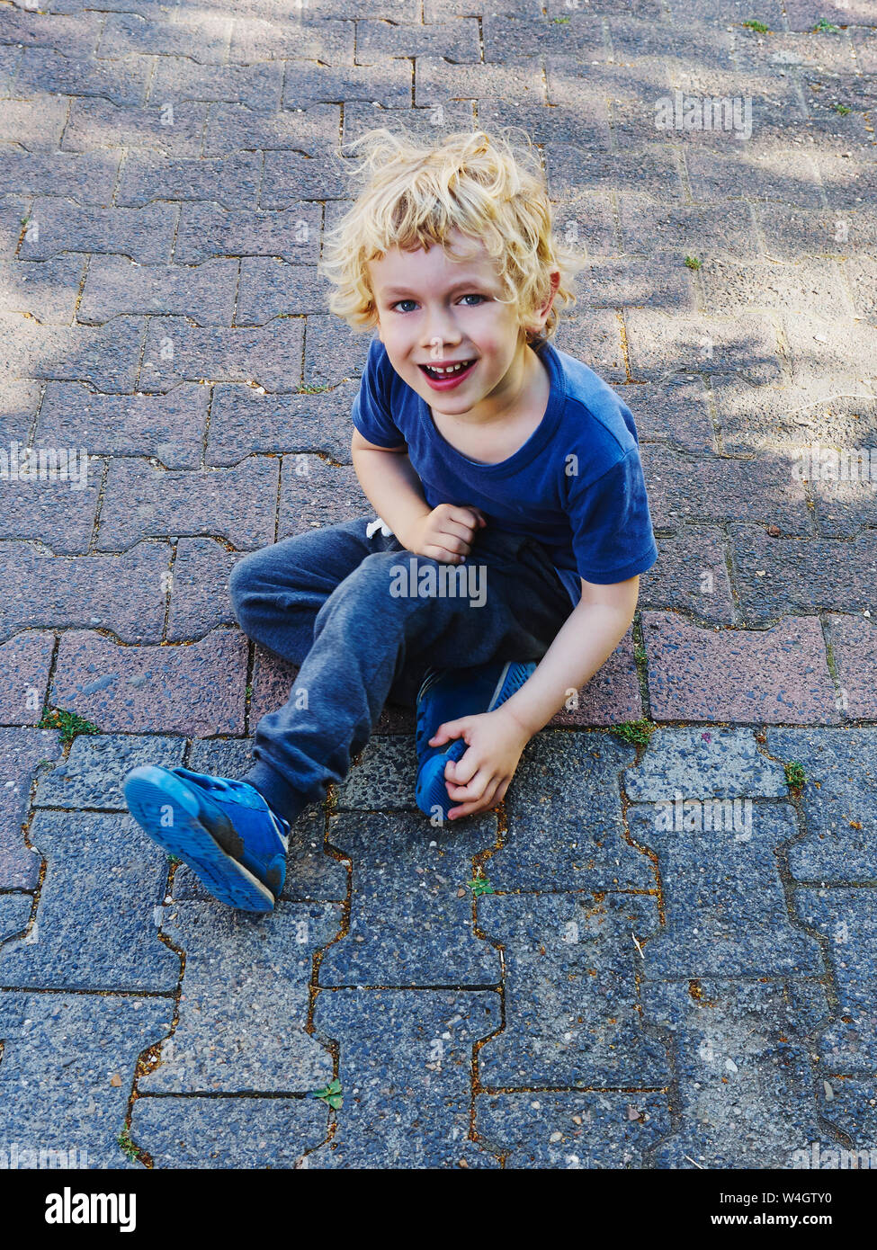 Portrait of smiling little boy dressed in blue sitting on pavement Stock Photo