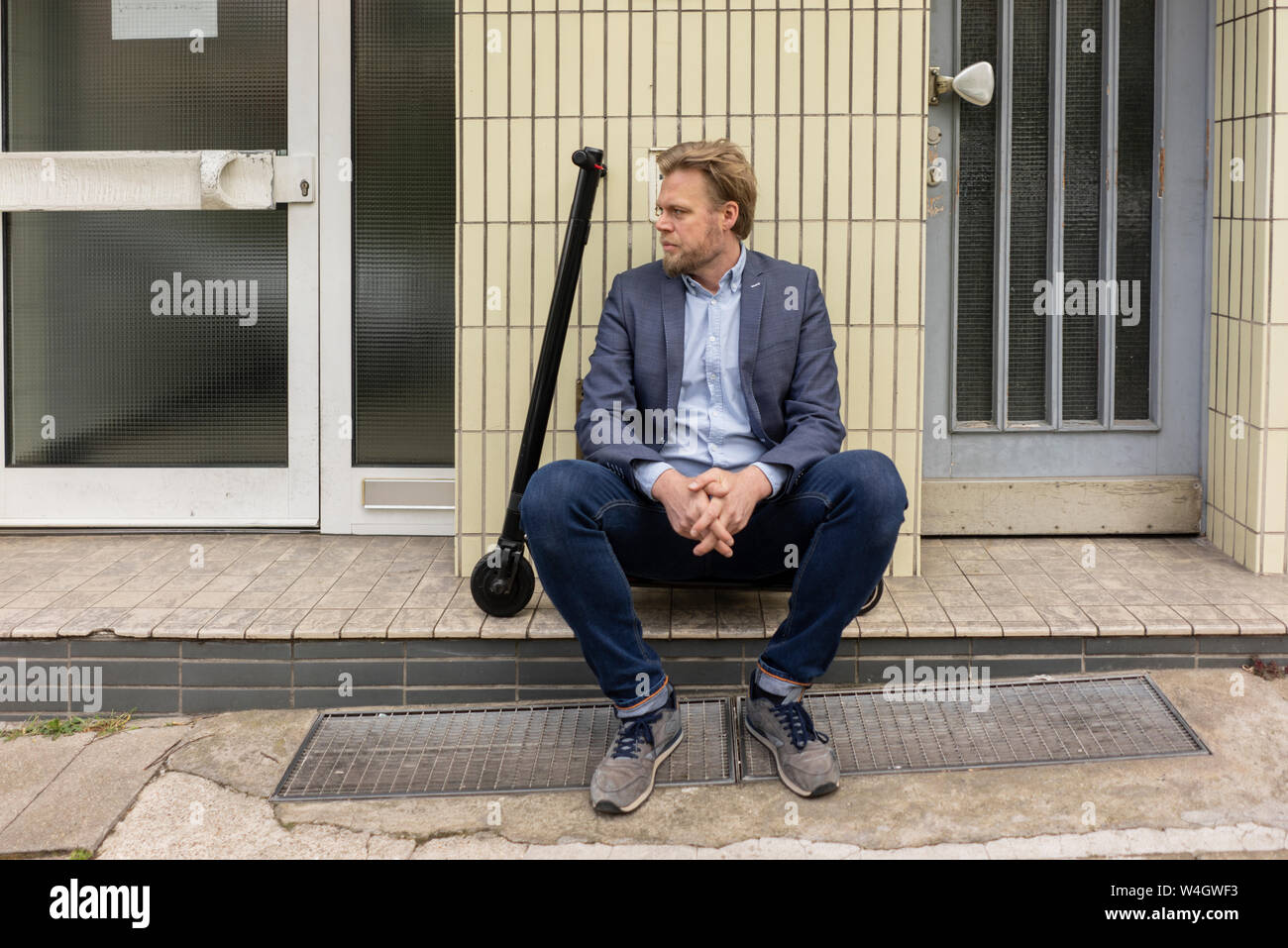Businessman with E-Scooter sitting on step in front of a house Stock Photo