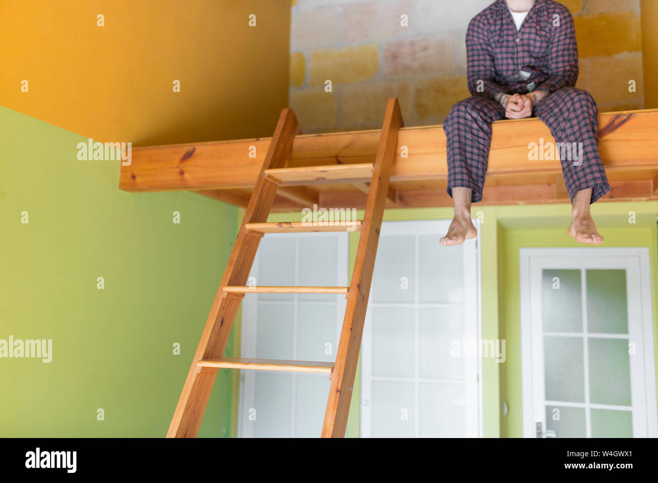 Man wearing a pyjama and sitting on loft bed at home Stock Photo