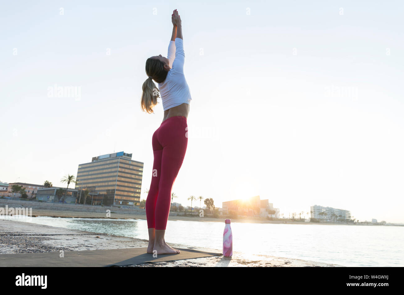 Young woman practicing yoga on the beach, doing sun salutations Stock Photo