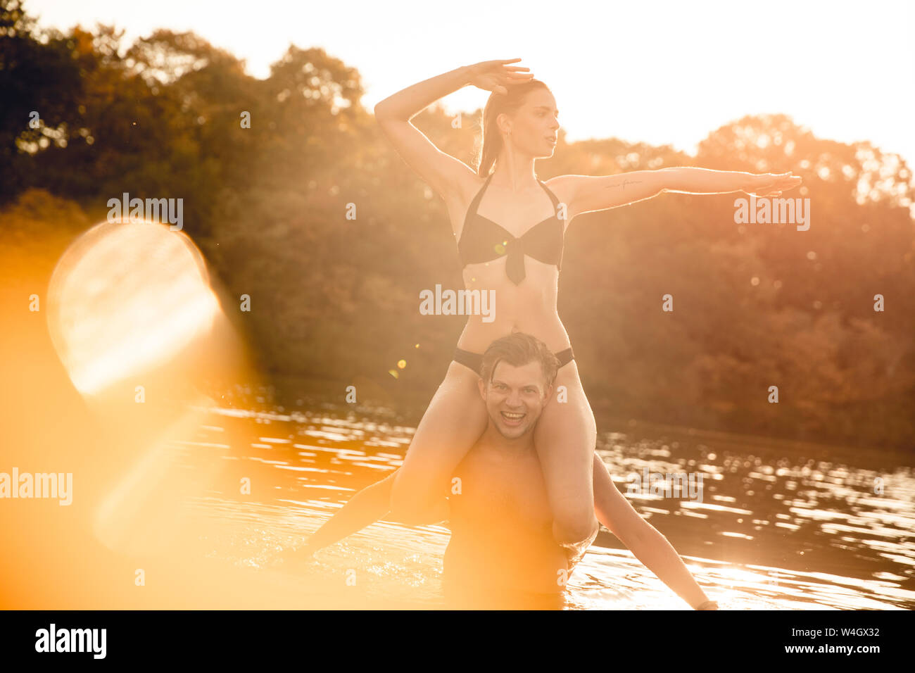 Young woman sitting on shoulders of young man standing in lake, enjoying the sun Stock Photo