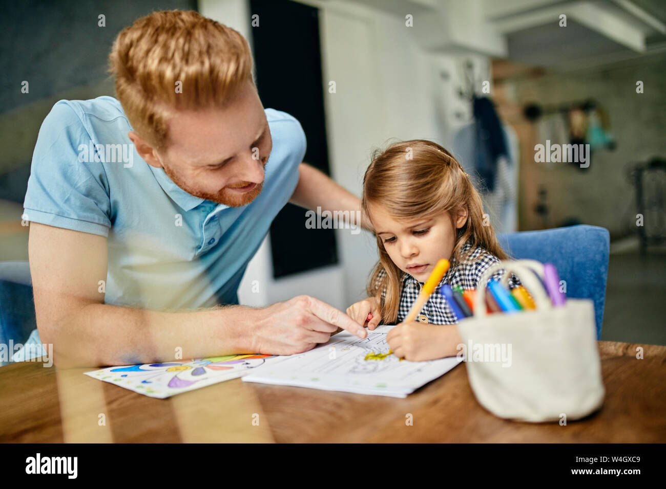 Father and daughter sitting at table, painting colouring book Stock Photo
