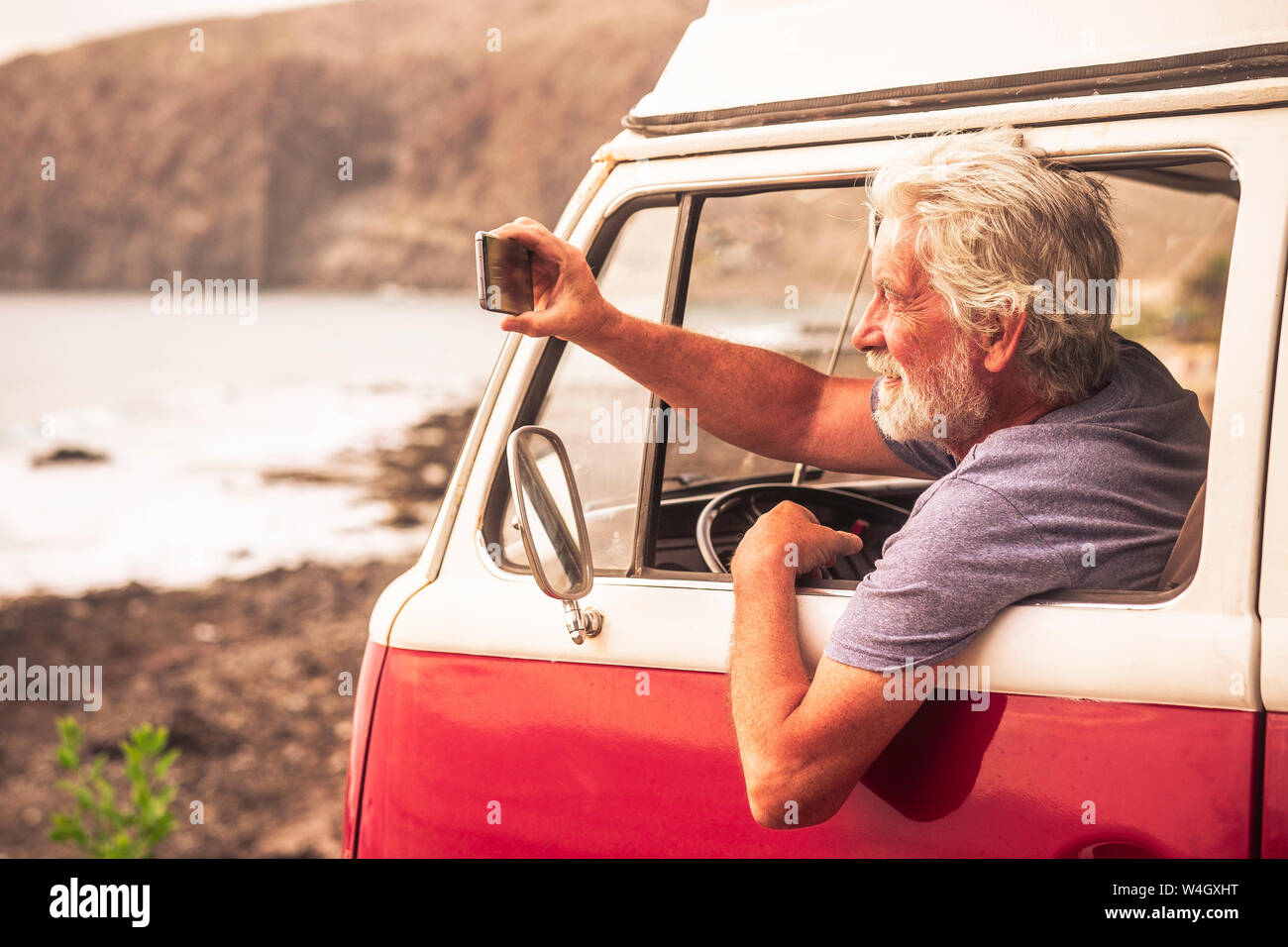 Senior man travelling in a vinatge van, taking pictures of the sea Stock Photo