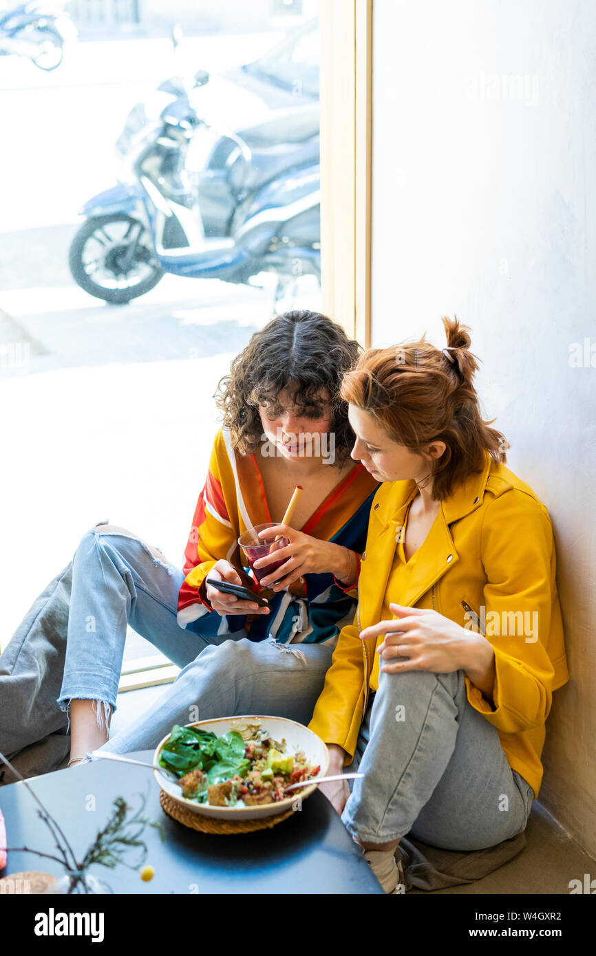 Two young women in a cafe looking at cell phone Stock Photo